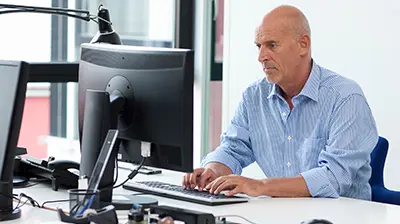 FIRST Canada and Applied Epic Integration Man in casual attire sitting at a desk in an office with two large computer screens in front of him.